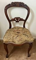 Front view of wooden balloon back chair showing carved floral crest and upholstered seat with floral tapestry fabric.