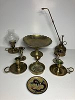 Assorted brass pieces including oil can, pedestal dish, lamp with chimney, candlesticks, and decorative dish