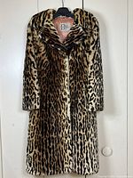 Front view of full-length vintage cheetah print fur coat hanging on black hanger against white background.