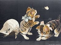Close view of embroidered artwork showing three kittens playing with a butterfly on black background
