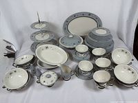 Full assortment including three-tier server, serving bowls, stacked plates, cups and saucers arranged on white drape