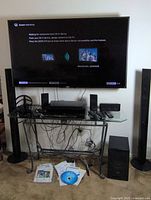 Full setup showing TV, speakers on stands, media players, headphones, power strip and cables