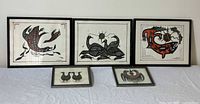 Five framed Indigenous art drawings are shown in one photo, arranged on a table.