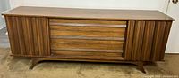 Front view of Princeville Mid-Century Modern dresser showing three central drawers and sliding doors on sides.