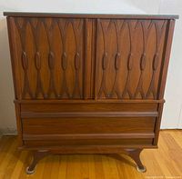 Full frontal view of the mid-century modern high boy dresser showing the carved wood front panels, drawers, and legs.