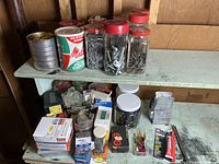 Overview of assorted hardware including glass jars, metal cans, boxes, and small containers filled with bolts, screws, nails, washers, and nuts.