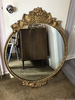 Full frontal view of the large ornate round mirror showing its wide gilded frame with leaf and grape cluster carvings.
