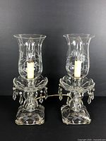 Pair of antique etched glass hurricane lamps with etched floral and grapevine detail, standing side by side with prisms hanging around the bulb holder area.