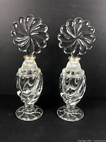 Pair of vintage Art Deco clear glass perfume bottles standing side by side with their swirl-petal stoppers inserted, showing overall shape and design.