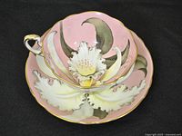 Cup nested in saucer showing pink interior and white orchid motif with gold trim