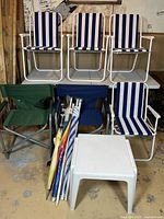 Overall view of all items including four striped folding chairs, two camping chairs, patio table, and umbrellas