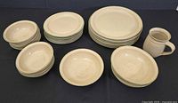 Full set of pottery dishware showing arrangement of dinner plates, side plates, bowls, small bowls and pitcher on dark backdrop.