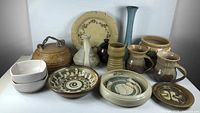Full view of assorted pottery including plates, bowls, vases, mugs, and lidded jar arranged on white table.