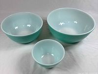 Set of three Pyrex bowls showing robin egg blue color with white interiors, arranged on white surface.