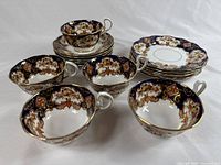 Five Royal Albert teacups grouped with matching saucers and dessert plates showing detailed floral and cobalt blue pattern with gold trim.