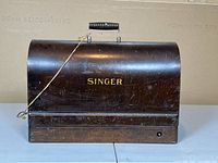 Locking wooden cover for Singer sewing machine with handle and gold lettering.