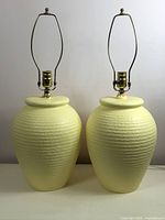Pair of yellow/cream colored textured plaster lamps with rib pattern, urn-like bases, brass hardware, and harps for shades.