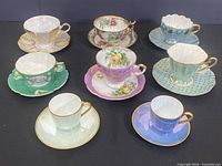 Eight assorted vintage porcelain teacups on matching saucers with various colors, patterns, and gold detailing, laid out on black background
