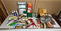 Wide view of all painting and tiling tools arranged on table showing paint rollers, brushes, sealant tubes, and hand tools