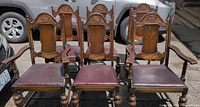 Front view of six vintage dining chairs including 2 captain's chairs with armrests, showing carved woodwork and leather upholstered seats.