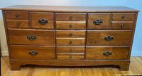 Full frontal view of the vintage wood dresser showing nine drawers, different handles, and wood grain texture.