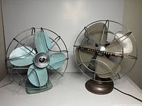 Two vintage electric fans side by side for comparison, one Electrohome and one Westinghouse fan.