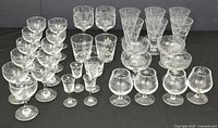 Front angle showing entire collection of etched glassware arranged in groups by style and size on black cloth.