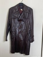 Front view of the vintage brown leather coat hanging on hanger, showing button closure, collar, and pockets.