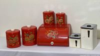 Full view of the vintage canister lot showing five red floral canisters, one bread box and two white labeled canisters