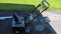Side view of Yardworks 12A electric snow thrower on paved surface, showing chute, wheels, and handle with cord.