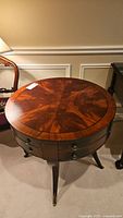 Front view of antique round wood table showing top surface, drawer pulls, and tapered legs with brass caps.