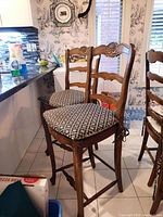 Two wooden bar stools with carved backrests and patterned cushioned seats, positioned next to kitchen counter.