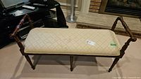 Front angle of wood framed upholstered bench showing cushion and carved armrests.