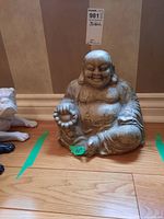 Front view of the 10-inch Buddha figurine sitting on a hardwood floor between two dog figurines.