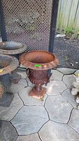 Full view of rust-colored cast iron planter with ornate base and rim.