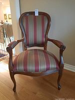 Front angle of wooden armchair showing striped upholstery and curved armrests.