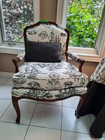 Front view of upholstered armchair with toile fabric and accent pillow in front of window
