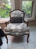 Front view of upholstered armchair showing carved wood frame and toile fabric upholstery