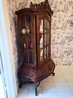 Side angle view of the wood china cabinet showing ornate carved top crown and glass-paneled door with visible shelves inside