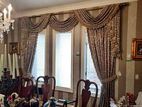 Curtains with swags draped above three windows, showing full arrangement in dining room.