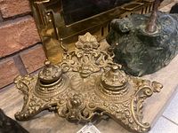 Angled view of the ornate metal desk set showing the two capped inkwells and detailed base.