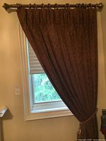 Brown drapes partially drawn with tasseled tiebacks around windows, showing fabric texture and rod finials.