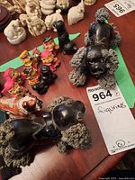 First photo showing black poodle dog figurines, colorful mini cartoonish figurines, and white or cream decorative miniatures in the background on wooden surface.