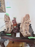 Two large carved wooden Foo dogs and smaller carved wooden frog sculptures displayed on an intricately carved dark wooden table; green measurement tags visible