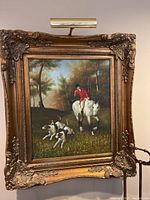 Full front view of framed print showing ornate gilt wood frame, hunting scene image, attached picture light