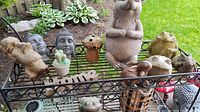 Wide shot of all garden figures and decorative items on metal rack, showing a variety of ceramic, resin, and wood items including a lion head sculpture and Buddha heads.