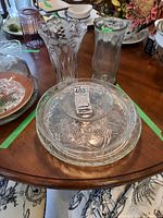 Two clear glass vases and three clear glass serving pieces including two plates and a bowl on a wood table