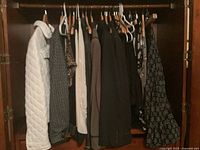 Photo of ladies clothing hanging on hangers includes jackets, pants and blouses in mostly neutral and dark colors