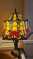 Close-up photo of the stained glass style lamp showing the colorful floral shade lit up and the detailed metal base.