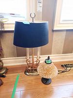 Tall lamp with brass base and black shade, smaller lamp with black base and yellow marbled glass shade shown together on floor near window.